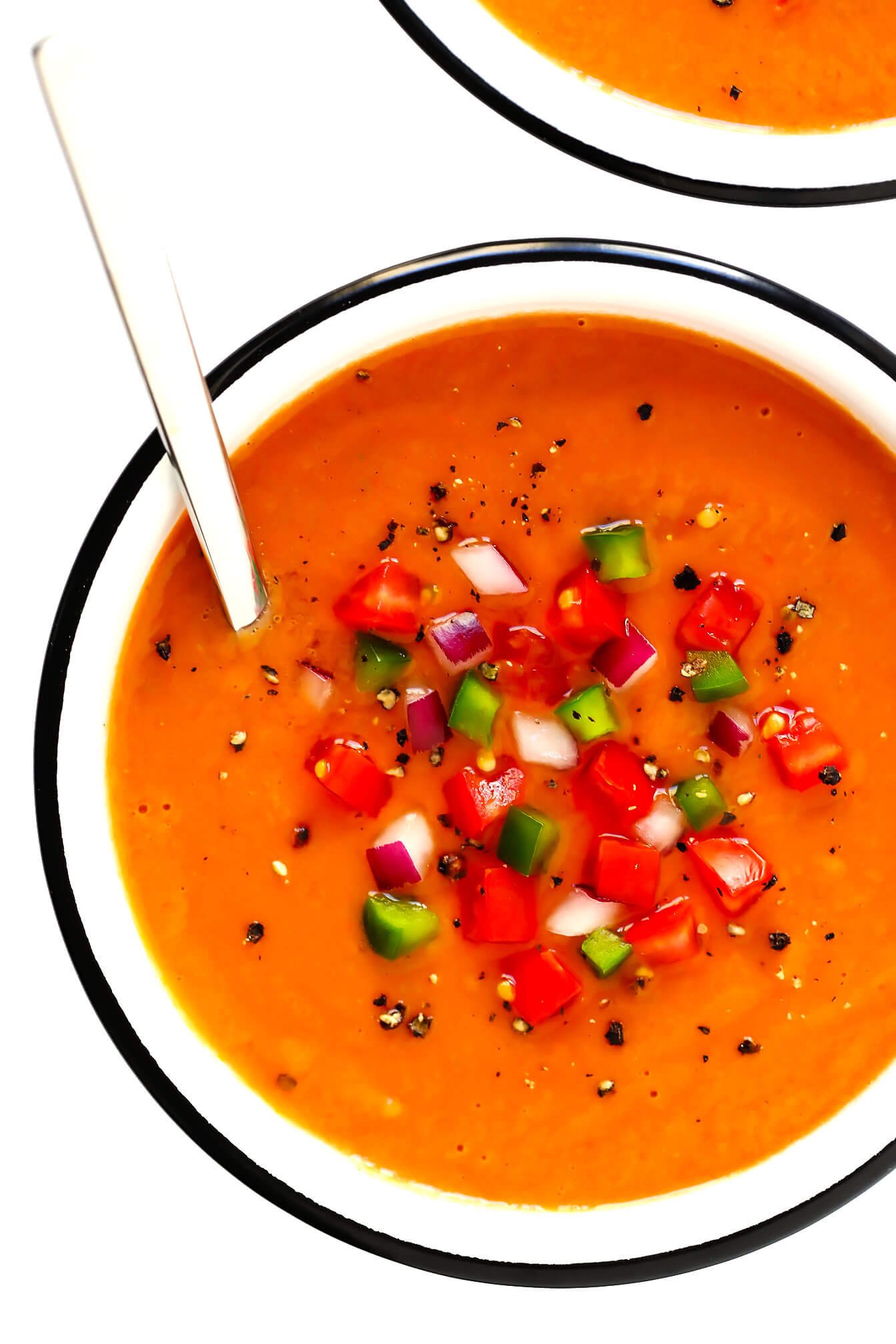 Bowl of Spanish gazpacho, topped with tomato, green pepper and red onion
