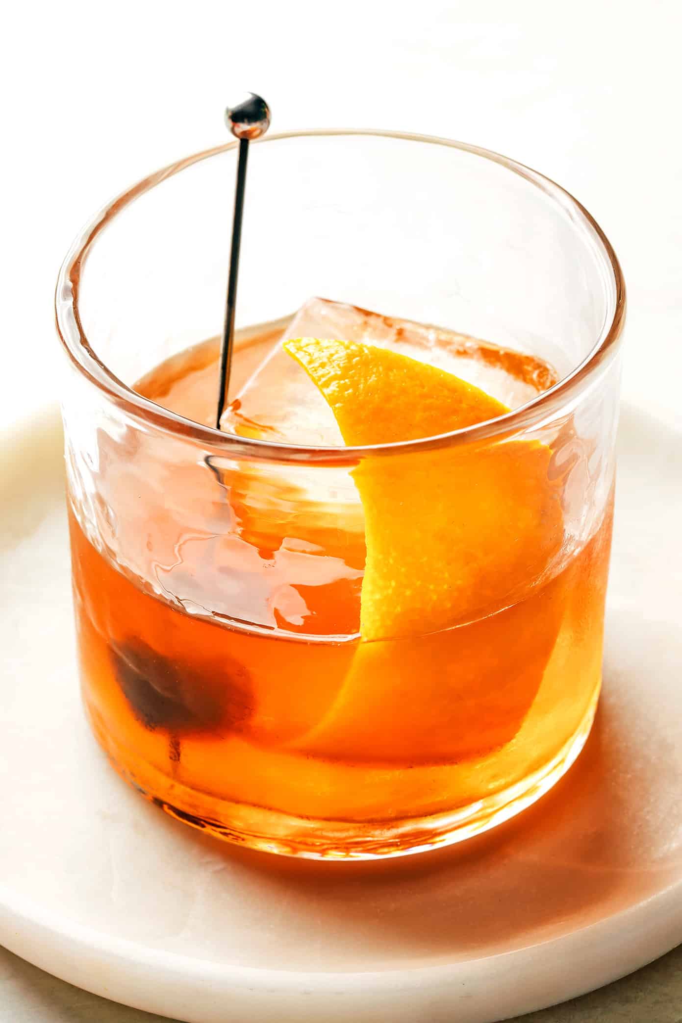 An old fashioned in a lowball glass with a large ice cube and an orange  peel