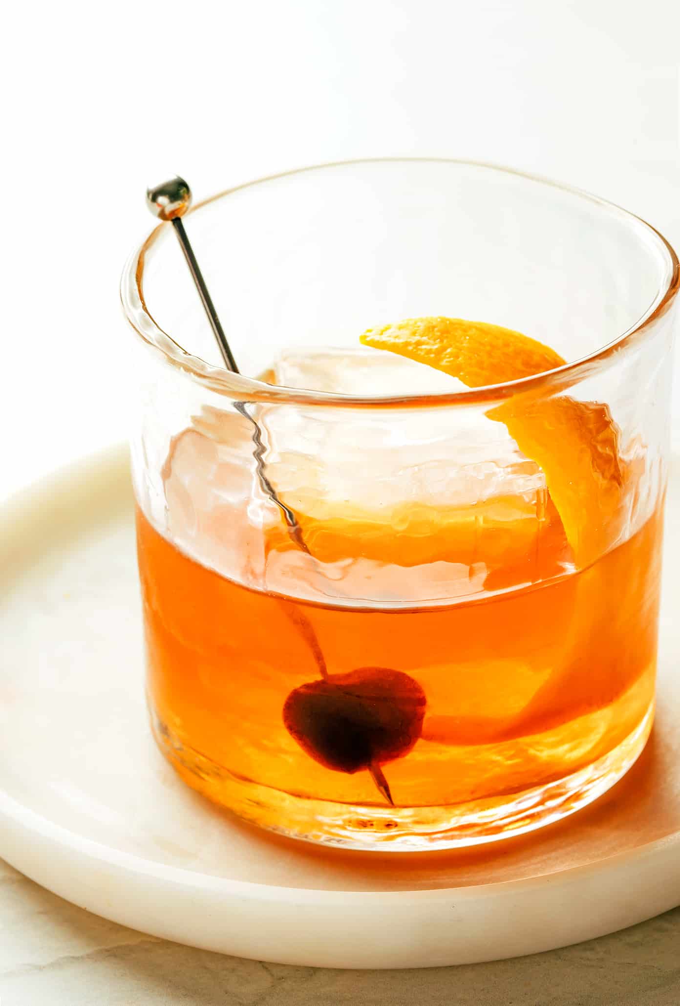 An old fashioned in a lowball glass with a large ice cube and an orange  peel