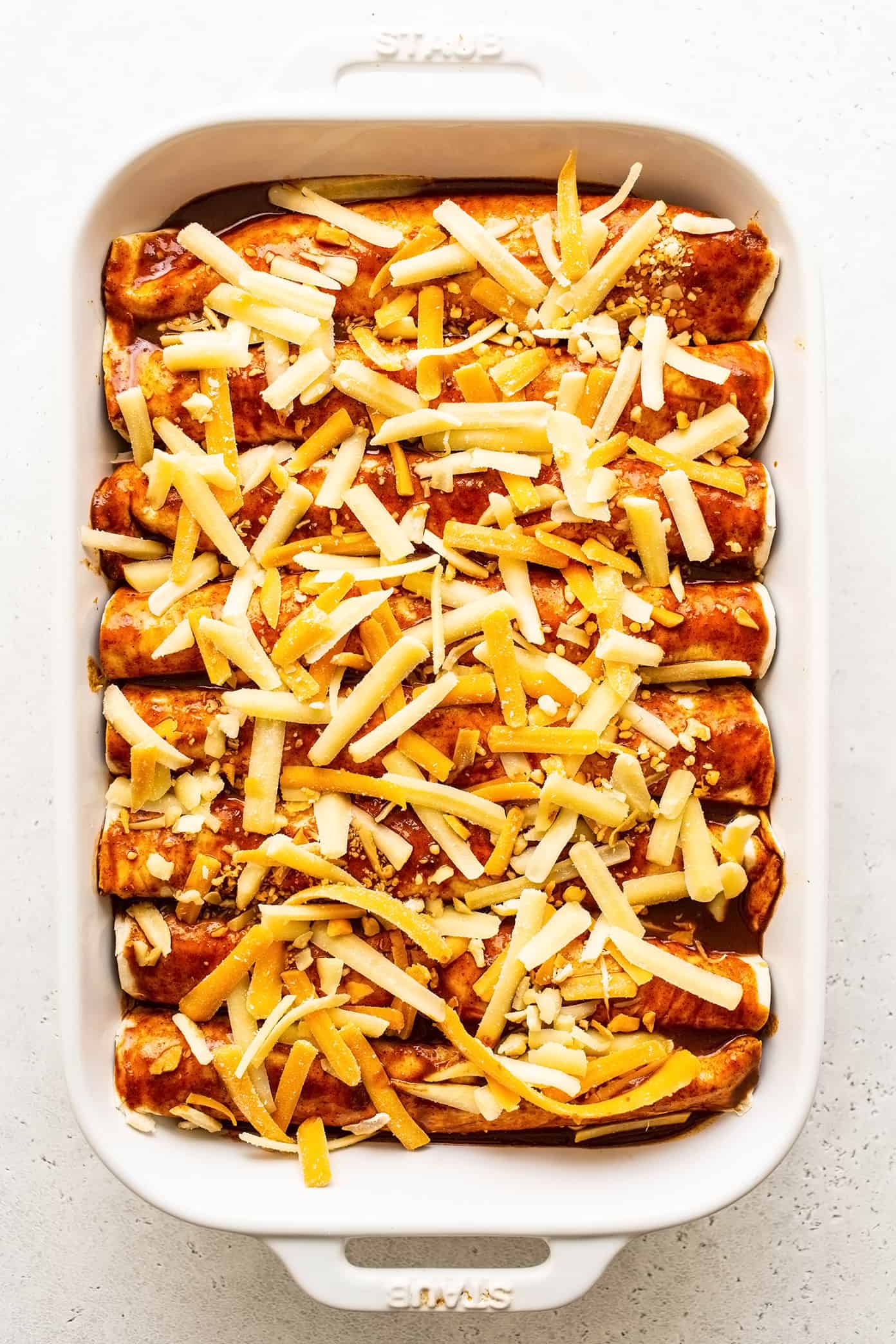 Uncooked beef enchiladas in pan with cheese