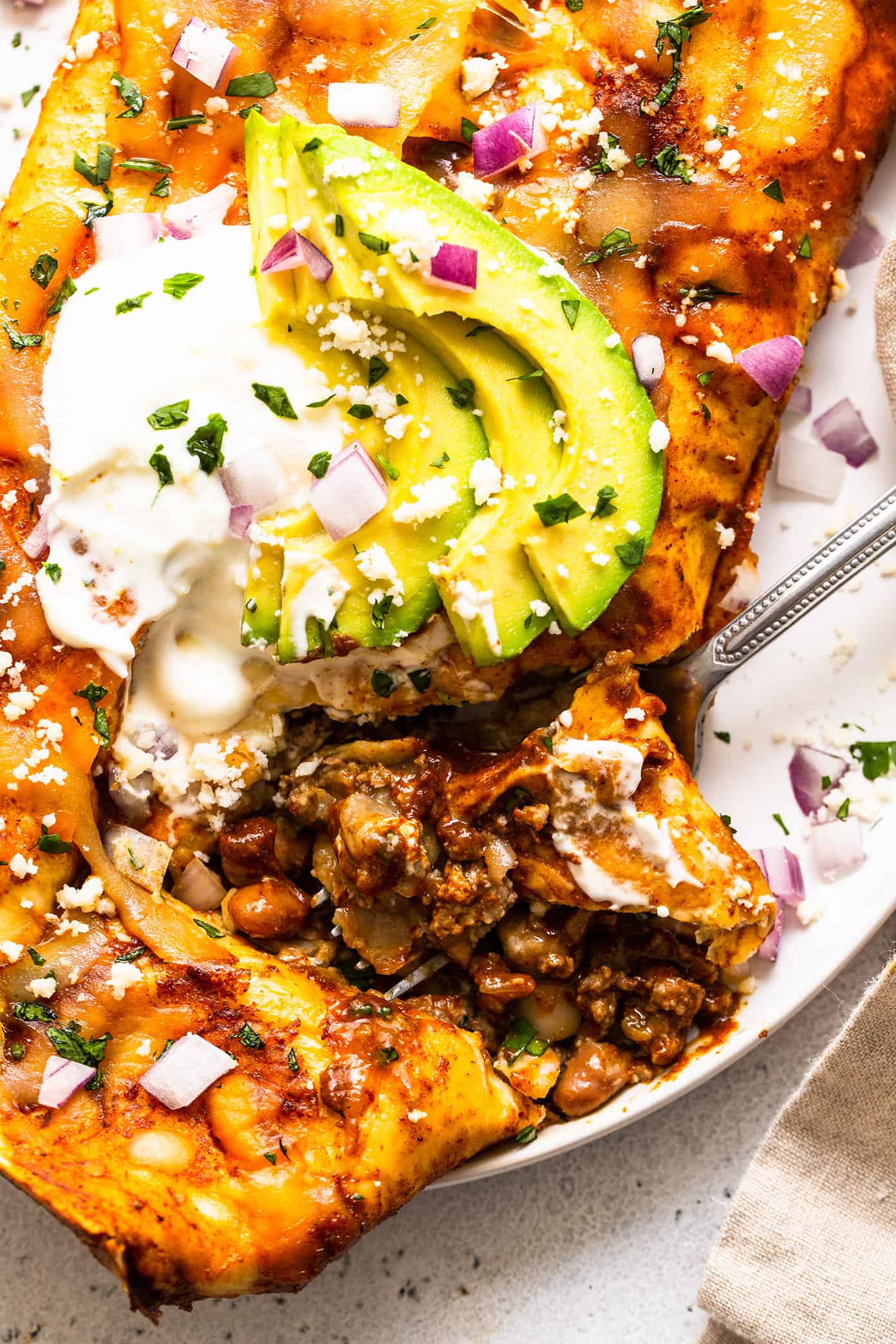 Beef enchilada closeup with avocado and sour cream