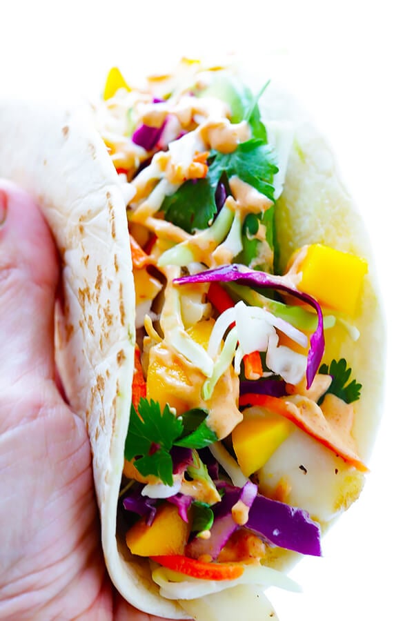 This Mango Chipotle Fish Tacos recipe is made with flaky mild fish, filled with a zesty mango slaw, and drizzled with a creamy chipotle lime sauce. So easy to make, and ready to go in less than 30 minutes! | gimmesomeoven.com