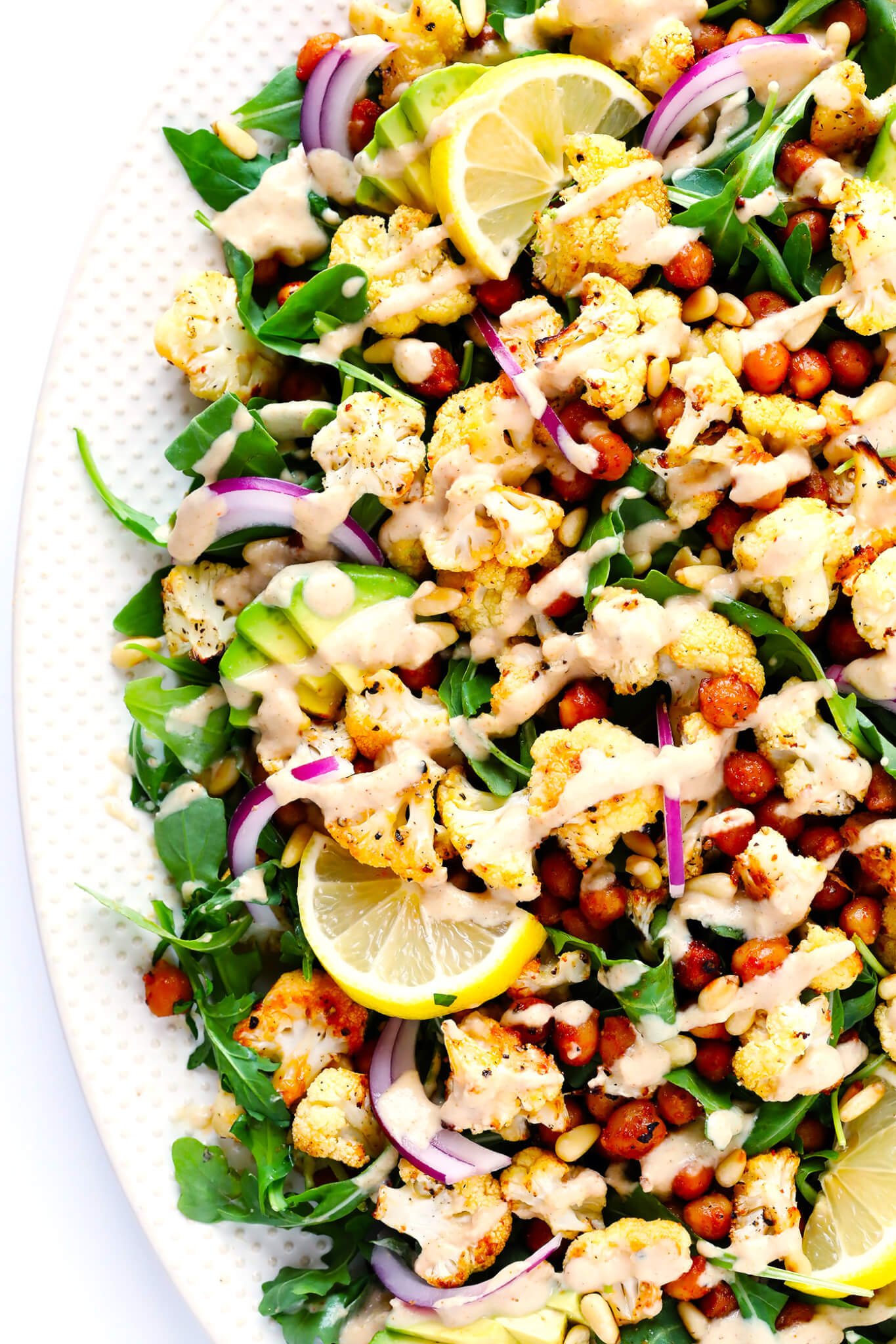 This Roasted Cauliflower, Chickpea and Arugula salad is tossed with a dreamy tahini dressing, lots of avocado, red onion, toasted pine nuts, and fresh lemon wedges. So delicious and easy to make! | gimmesomeoven.com (Vegetarian / Vegan / Gluten-Free)