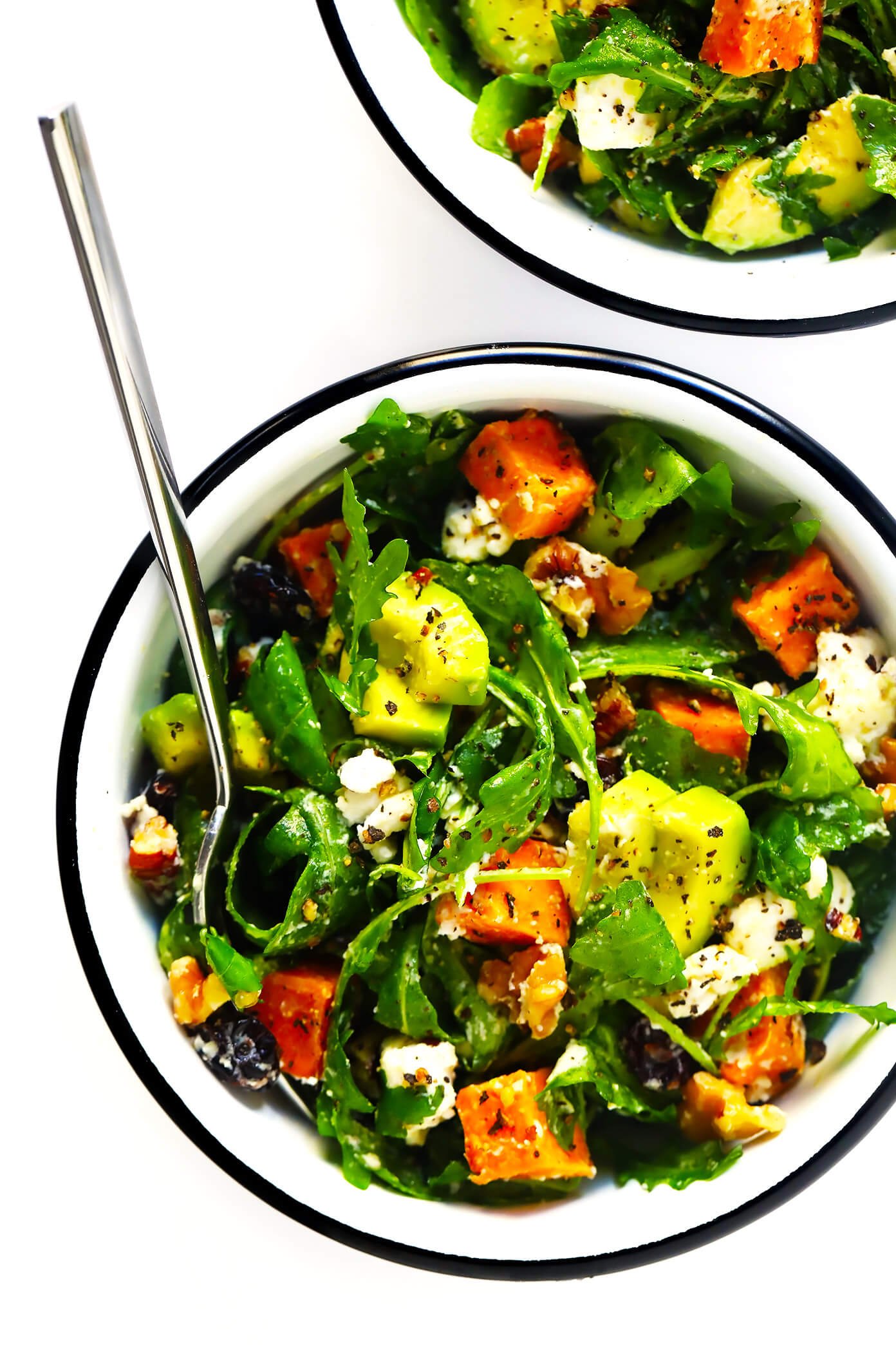 Image shows two bowls of salad topped with avocado and feta cheese