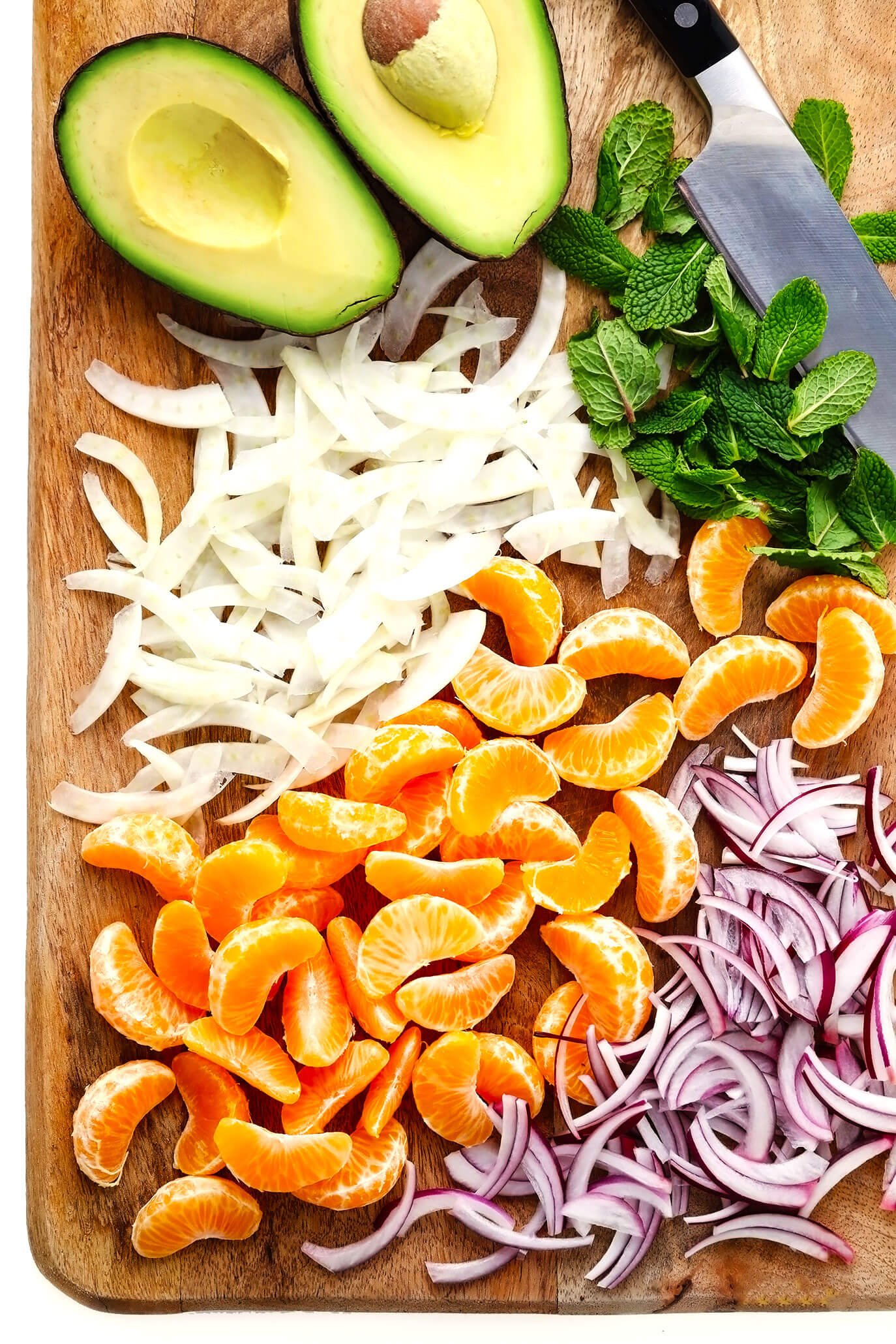 Cutting board with fresh avocado, fennel, red onion, mint and clementine oranges