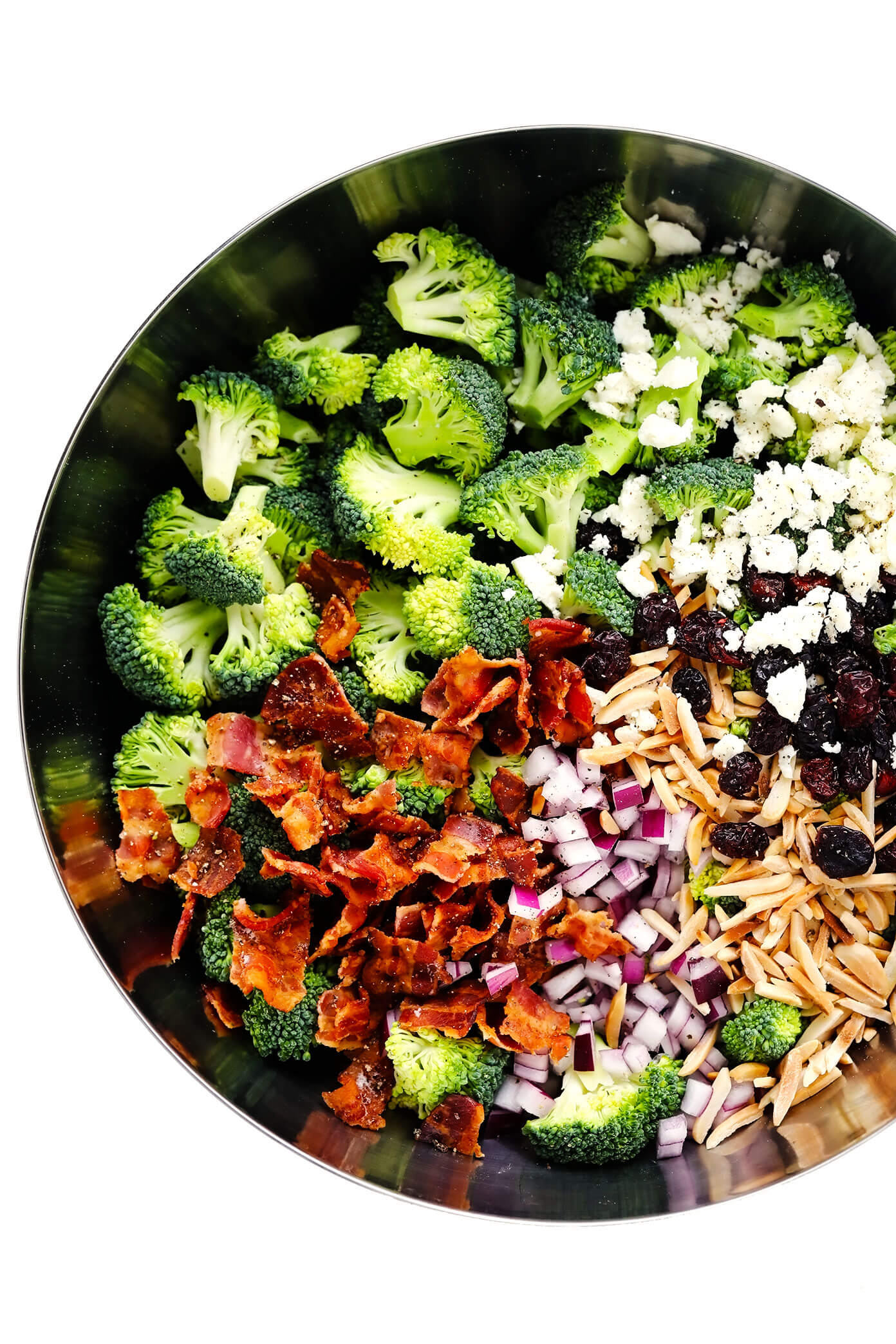 Ingredients for broccoli salad in a bowl - broccoli florets, bacon, red onion, toasted almonds, dried cranberries and feta cheese