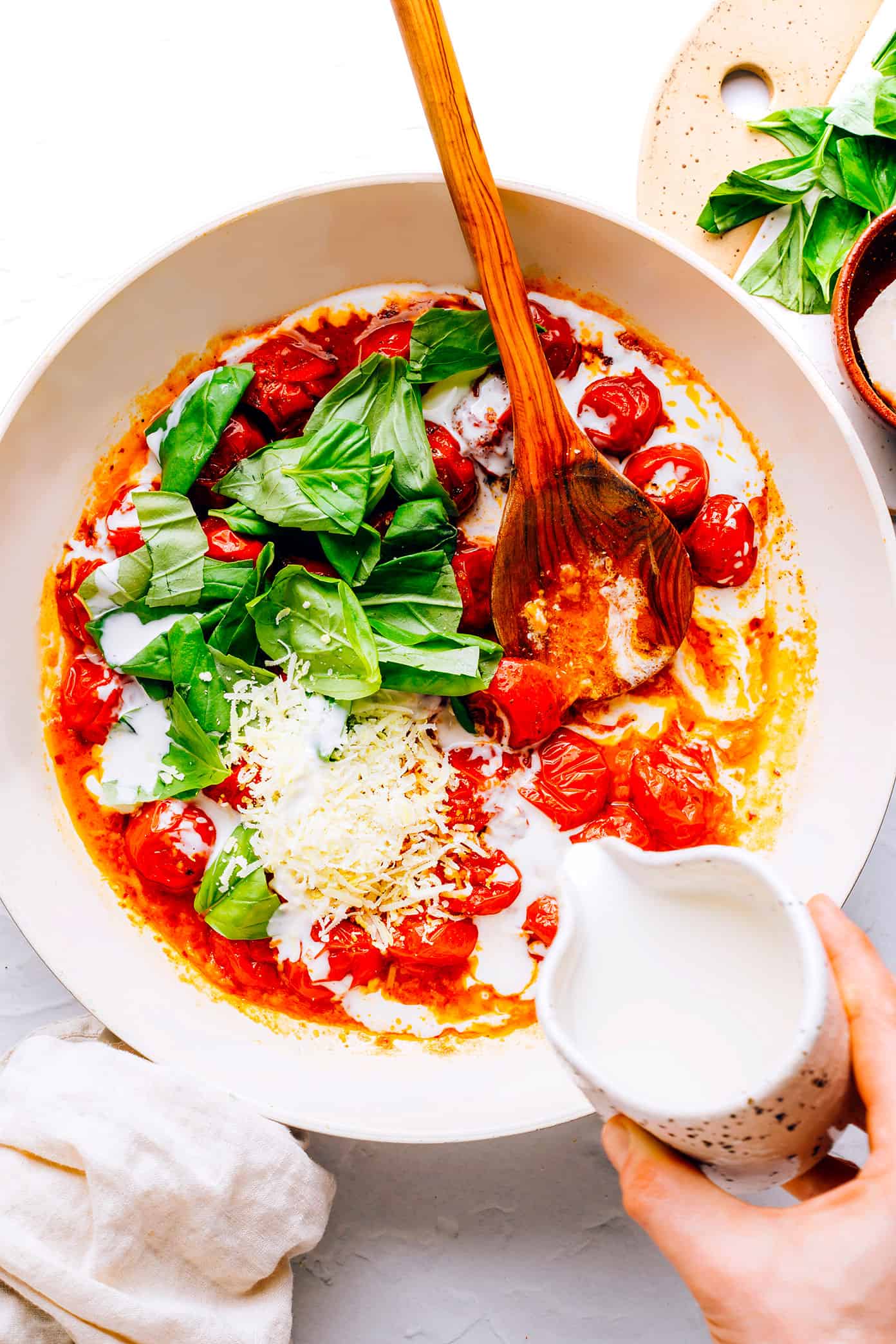 Adding cream to burst tomato sauce with basil