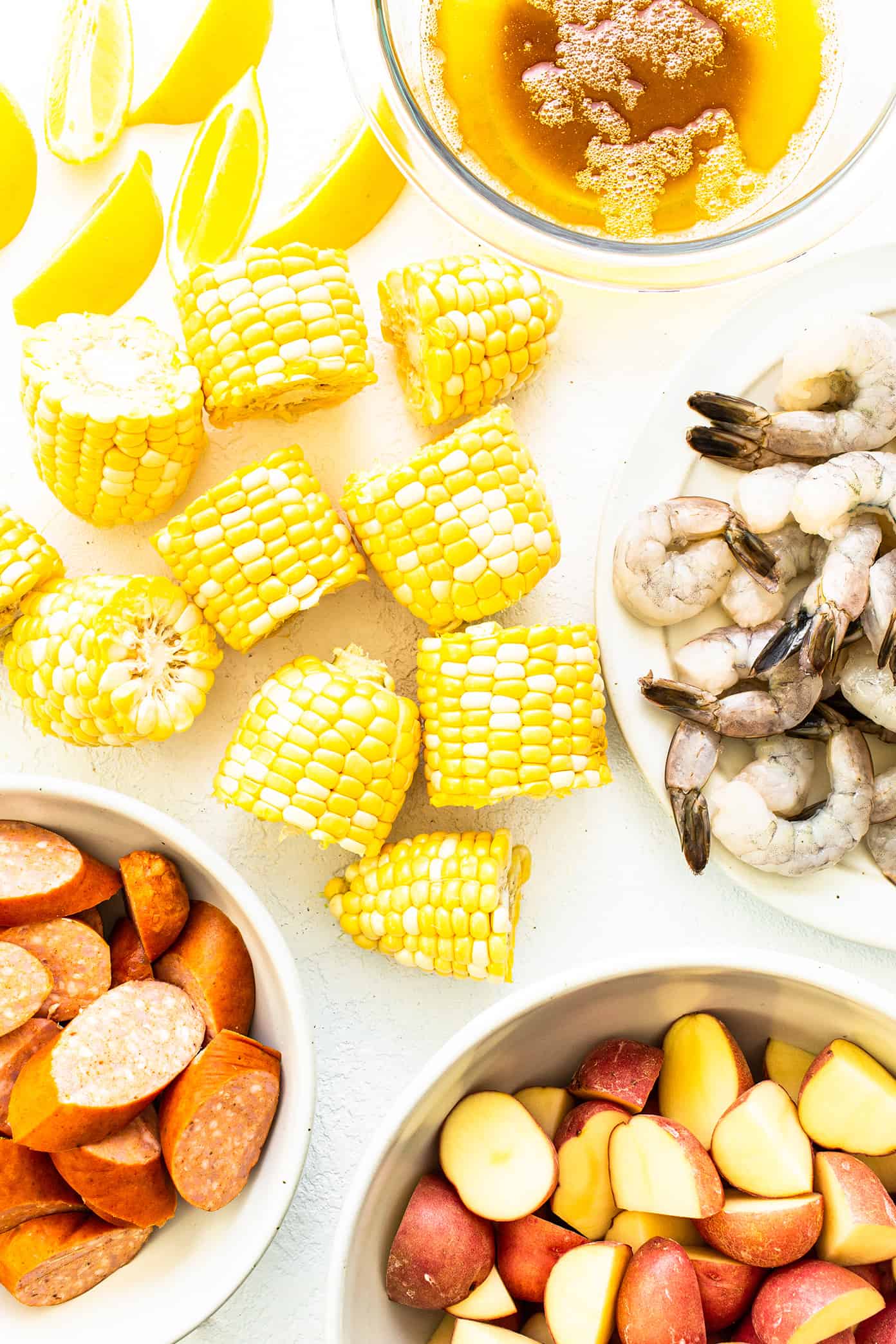 Ingredientes do cozimento de camarão (limão, espiga de milho, camarão cru, linguiça Andouille, batatas vermelhas, manteiga marrom)