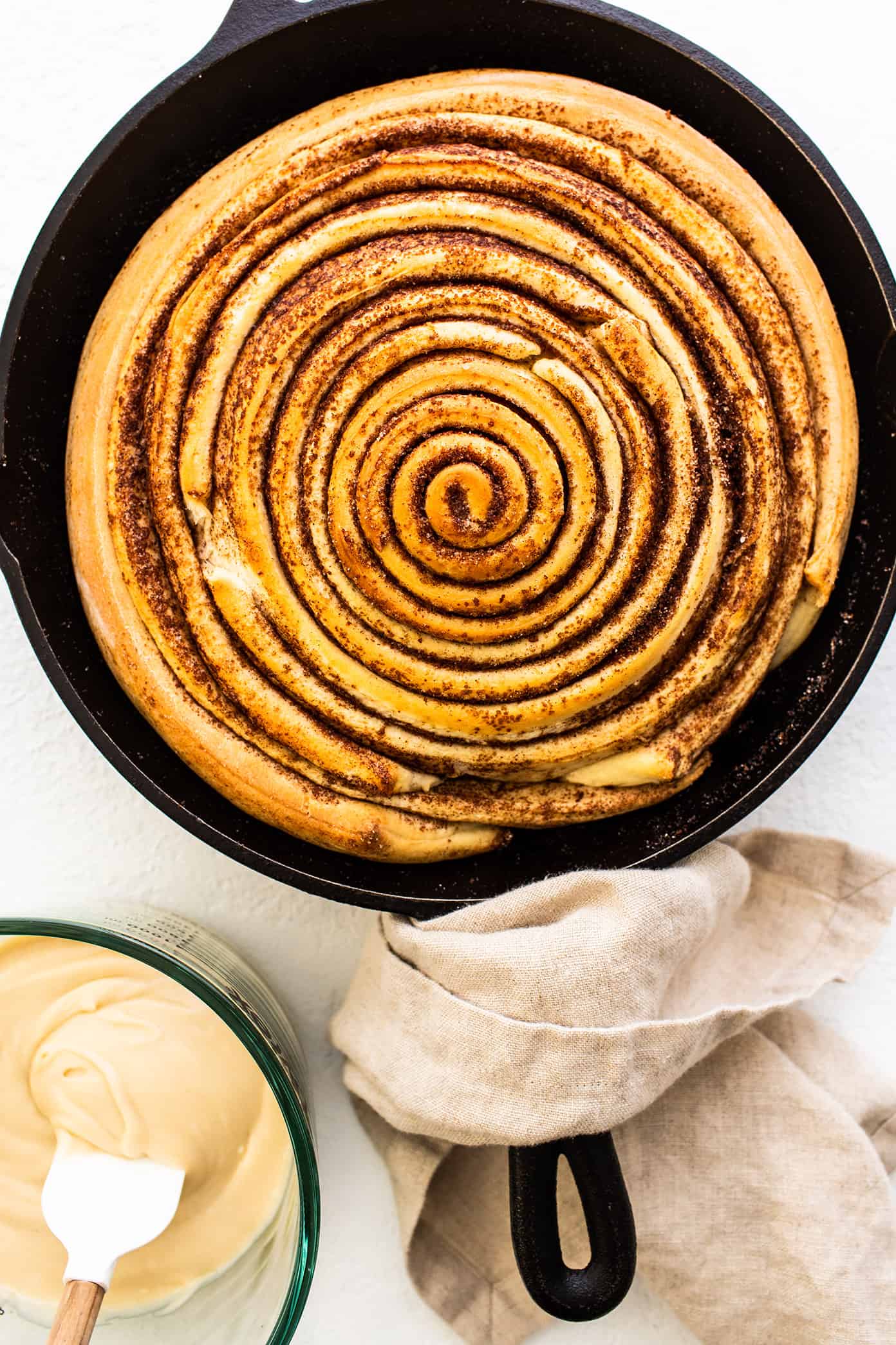 Unfrosted giant cinnamon roll in skillet with cream cheese frosting