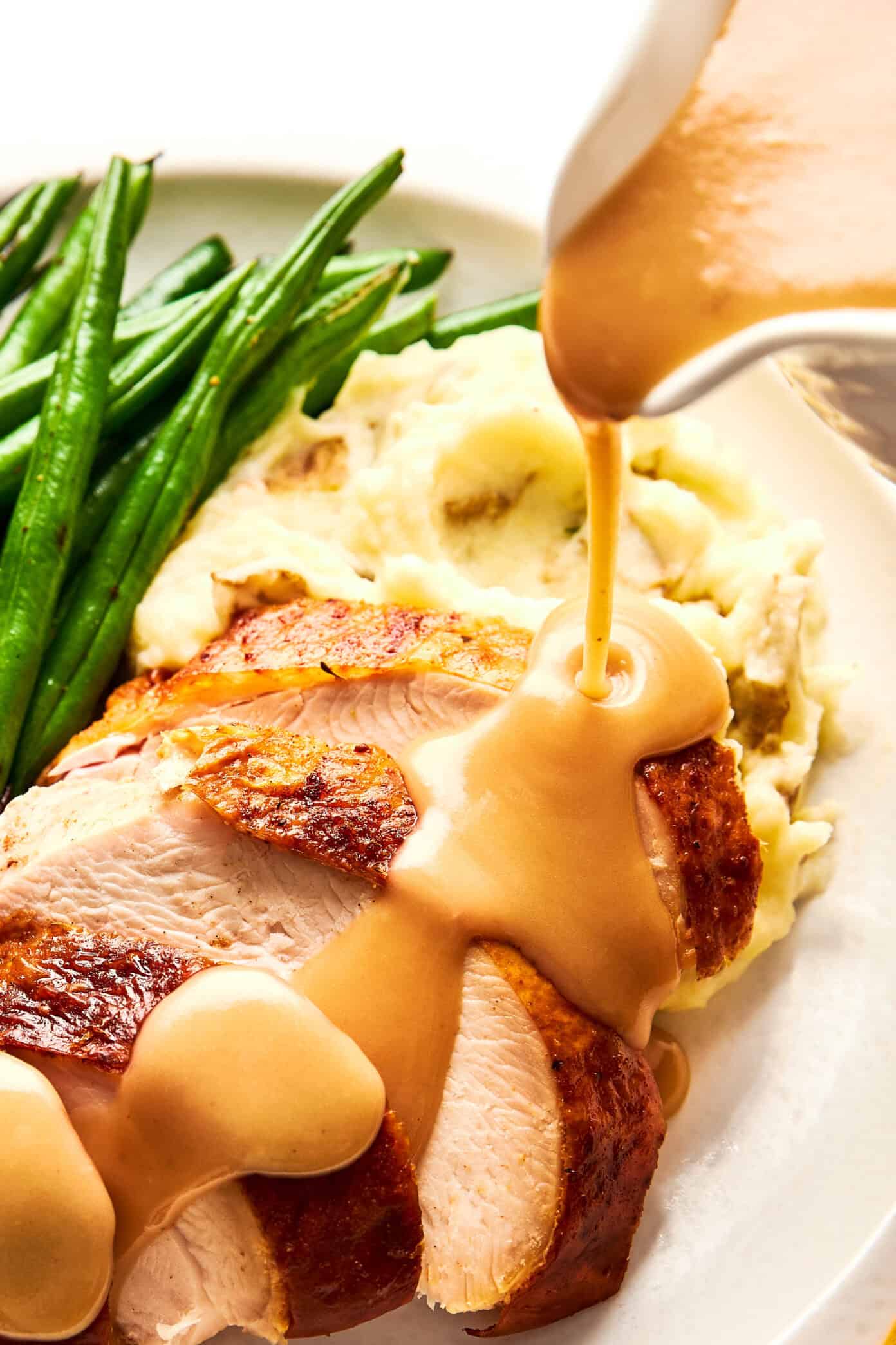 pouring turkey gravy over turkey and mashed potatoes
