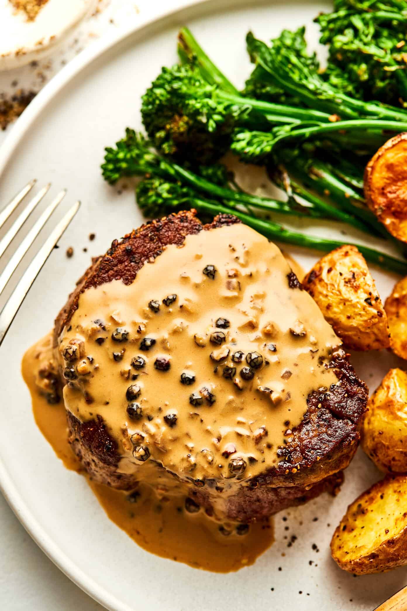 steak with peppercorn sauce on plate with broccolini and roasted potatoes