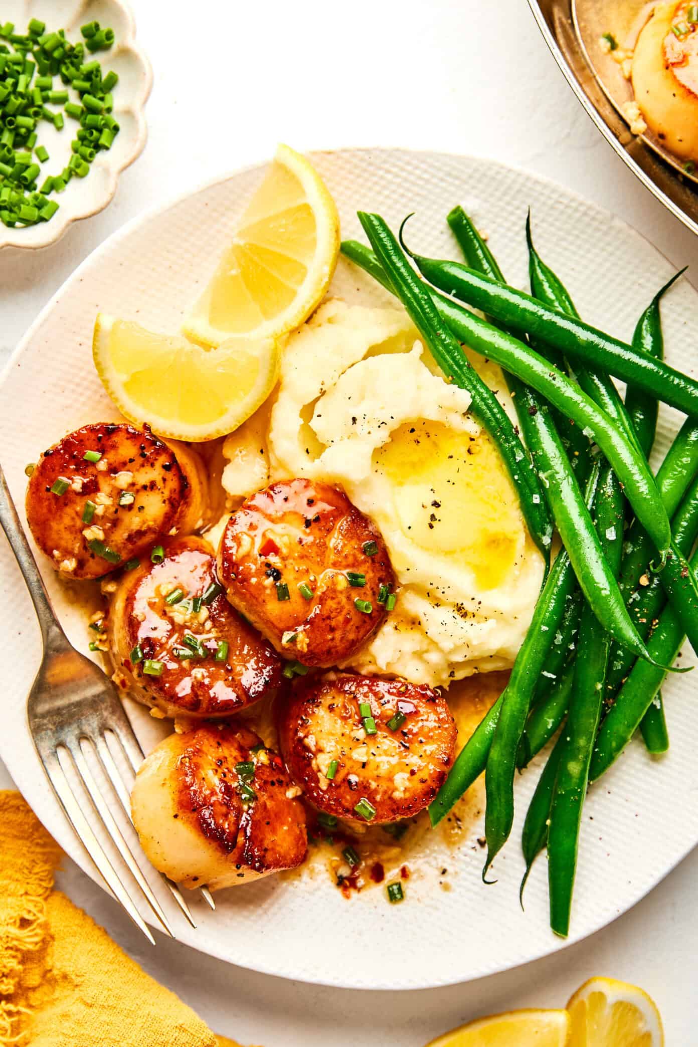 seared scallops dinner on a plate with mashed potatoes, green beans and lemons